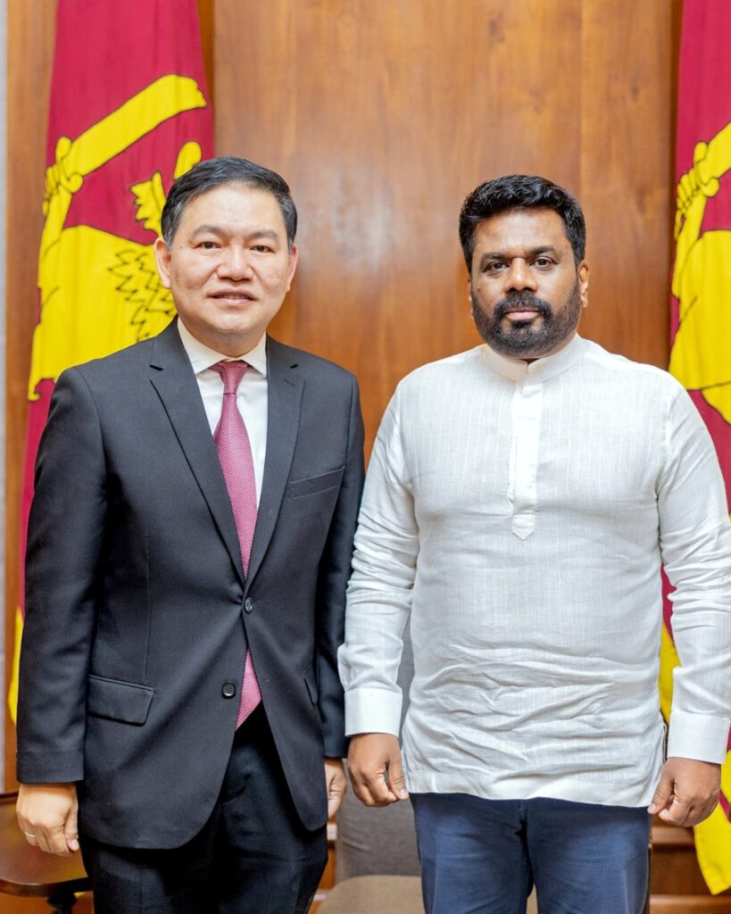 The Ambassador of Thailand with a Sri Lankan dignitary in front of Sri Lankan flags